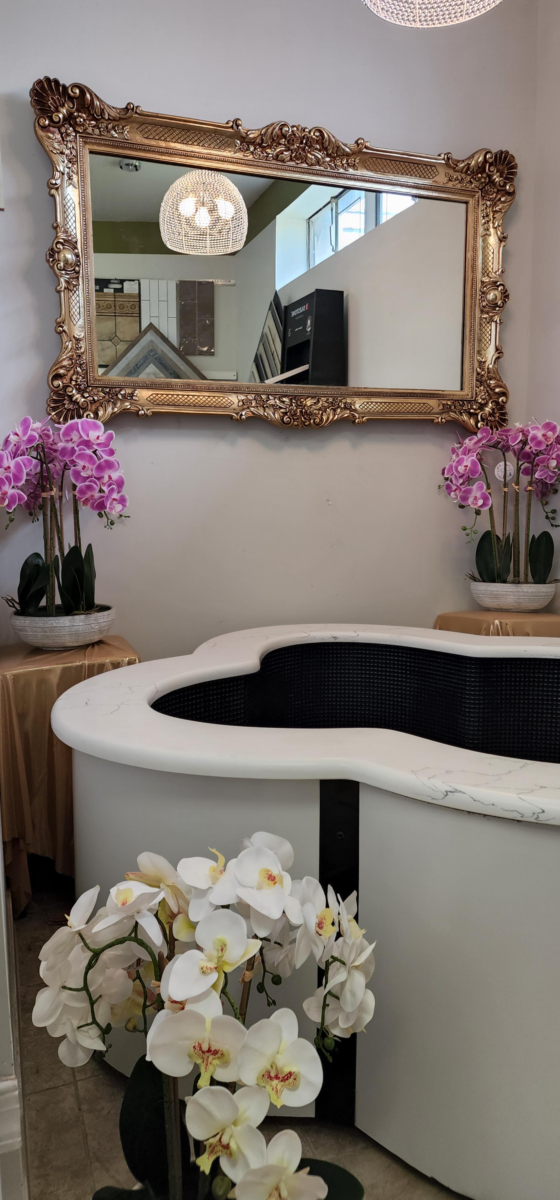 An irregularly shaped white modern bathtub with glistening blue tiles displayed in front of pink flowers in decorative pots.