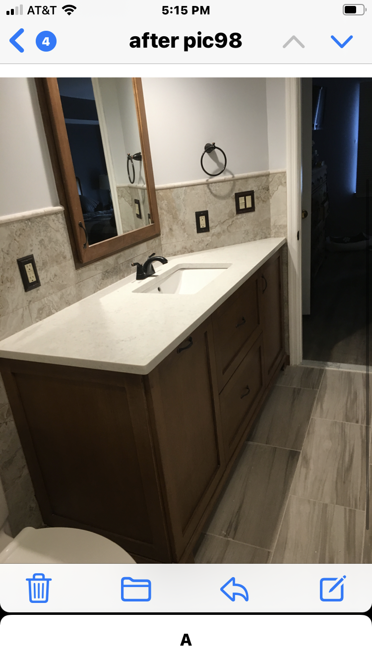 A brown wood bathroom vanity with single sink and marble countertop set in front of a stone backsplash.