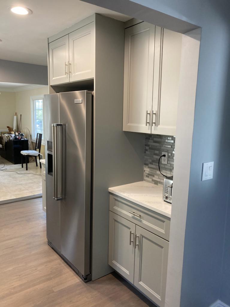 White kitchen cabinets and a stainless steel double door refrigerator adjacent to a room with a blue painted wall.