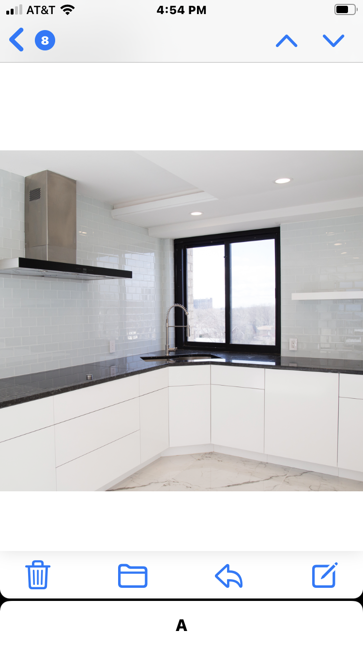 A sleek white kitchen with white tile backsplash, a stainless steel range hood and a black countertop and window trim.