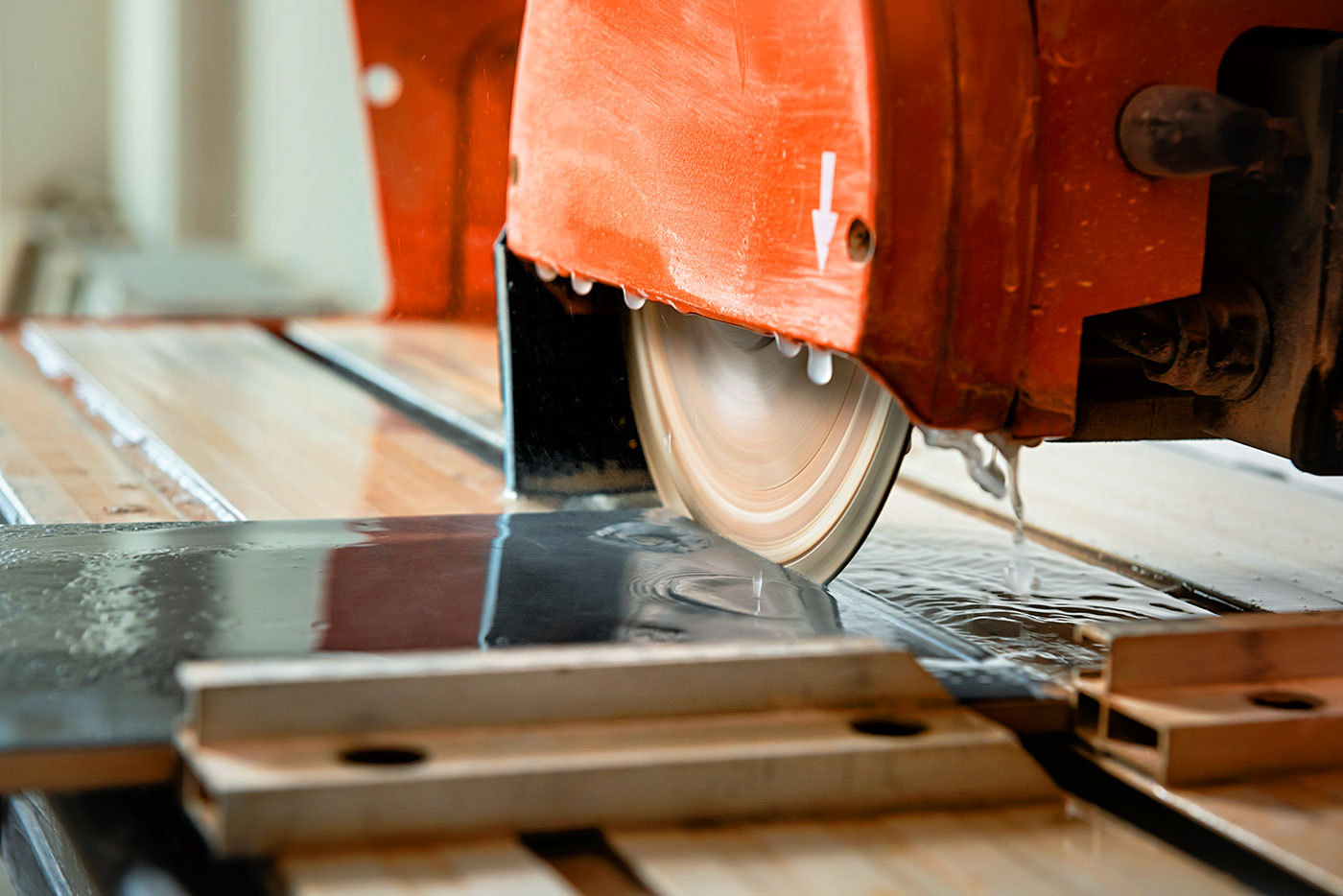 A wet saw on a table cutting into a piece of tile.