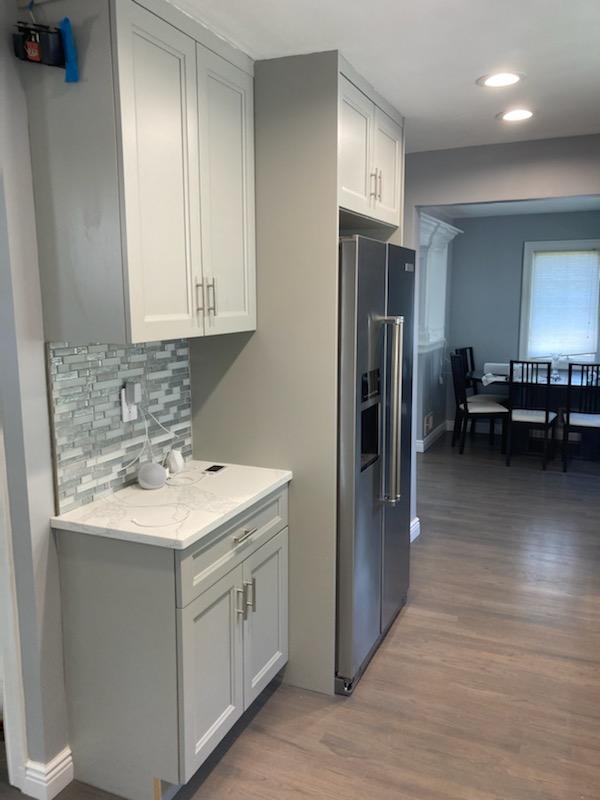 White kitchen cabinets with a gray and white tile backsplash and a stainless steel double door refrigerator.