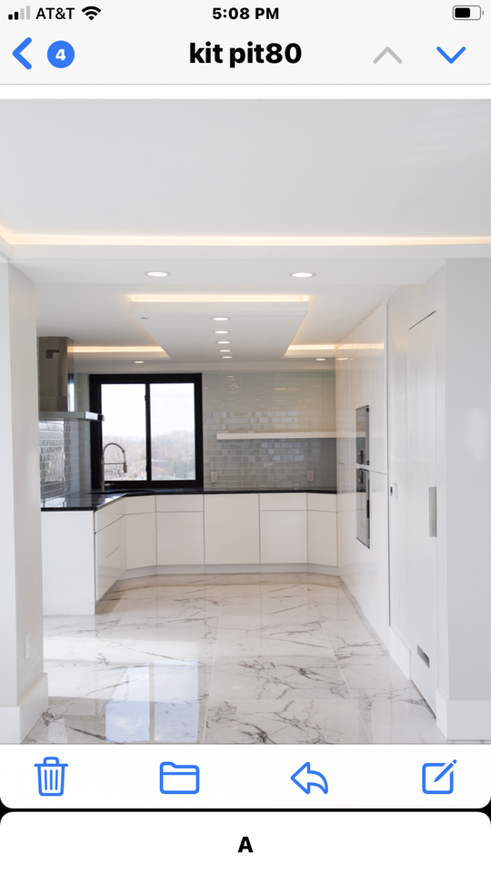 A sleek and clean, white marbled kitchen with a stainless steel range hood, white cabinets and backsplash and a black countetop.