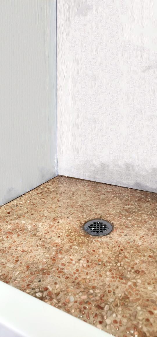 A close-up of the shower base with rock flooring and gray-white tiled walls.