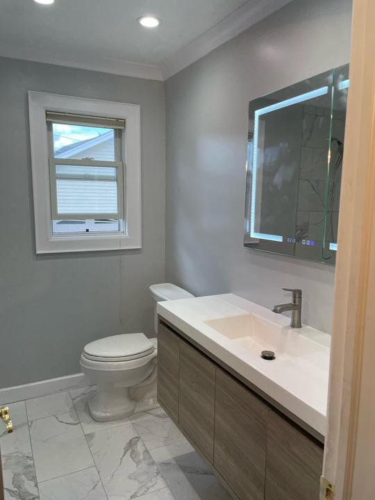 A modern bathroom with a white marble tile floor, crown molding and a light brown floating bathroom vanity sink.