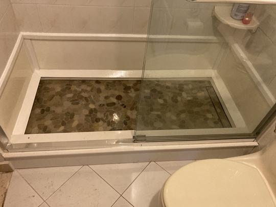 A stone shower base with a clear glass sliding door.