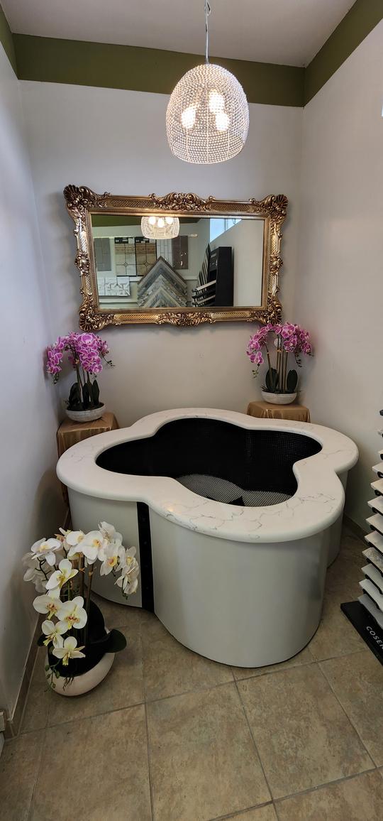 An irregular shaped white marble ledged bathtub with pink flowers in the background.