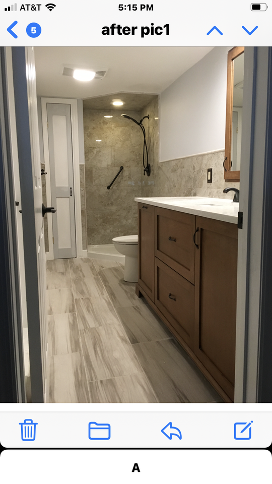 A brown wood bathroom vanity with pull out drawers and a cabinet set next to a stone tiled stand-up shower.