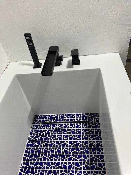 A blue and white rectangular shaped bathtub with black fixtures.