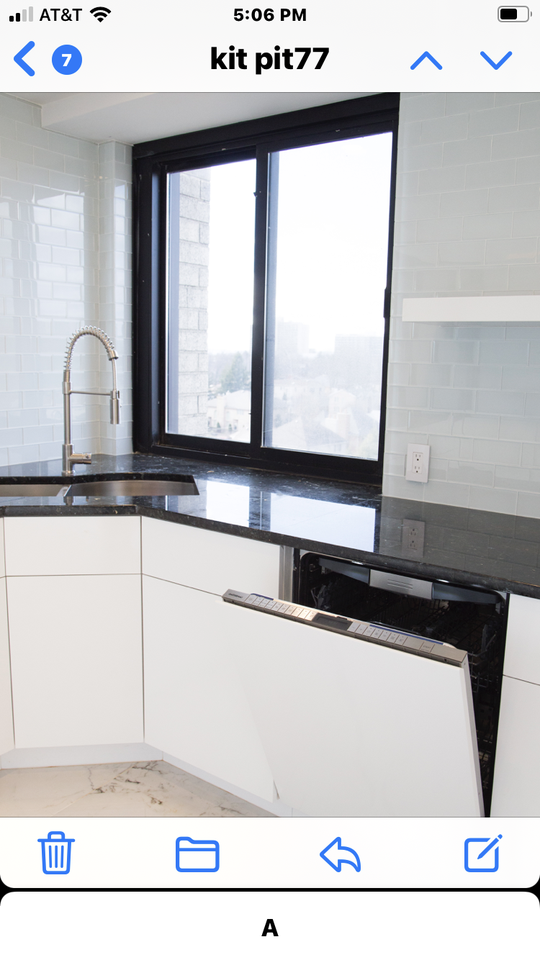 A white kitchen with white tile backsplash, stainless steel sink and black window trim and countertop.