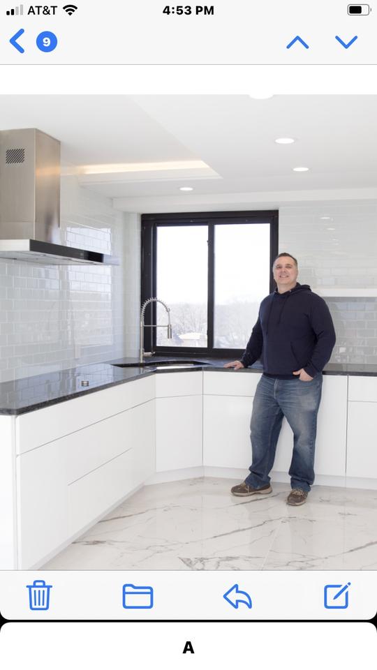 A person wearing a dark blue sweatshirt and blue jeans standing in a white and black modern kitchen.