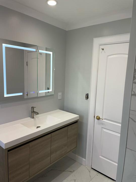 A white and gray marble bathroom with a light brown floating vanity sink and a decorative light-up mirror.